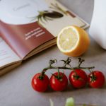 Flat lay of cooking ingredients including tomatoes and a lemon with a cookbook.