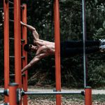 A shirtless man demonstrates strength and agility on outdoor calisthenics bars.